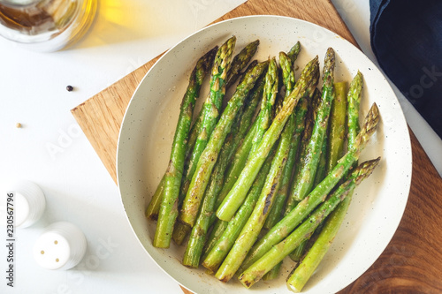 Top view on roasted asparagus in a white pan on a kitchen table. Modern style, vegetarian food.