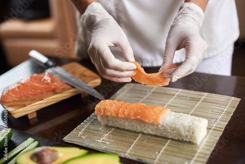 Close-up view of process of preparing rolling sushi with disposable gloves on bamboo mat