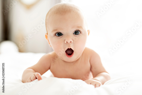 A Cute baby girl on a white bed at home yawn