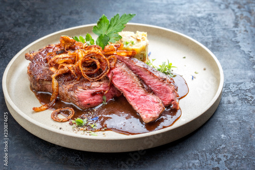 Modern design dry aged sliced roast beef with fried onion rings and mashed potatoes as closeup on a plate with brown sauce