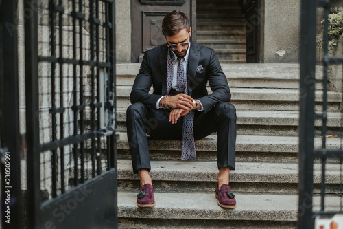 Businessman waiting on the stairs and looking at the time