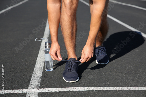 Sporty man tying shoelaces before running at stadium on sunny morning