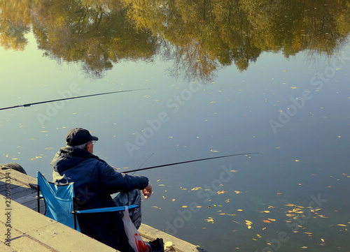 Fisherman with fishing rods catches fish in a river while sitting on the embankment on an autumn warm day