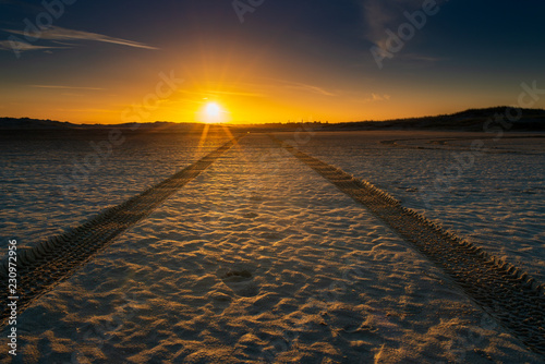 Sunset on the Harrington Sand Dunes. Footprints and tyre tracks lead off into the sunset.