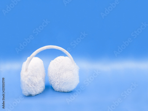White winter headphones for the ears on a blue background. MINIMAL COMPOSITION 