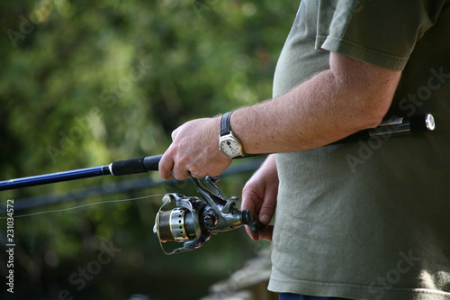 A close up of a man holding a fishing rod standing on a river bank fishing