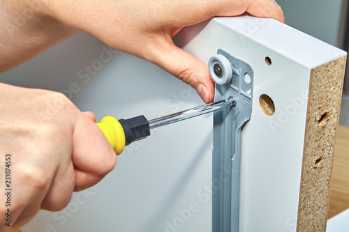 Furniture assembler tightens screw in drawer slides.