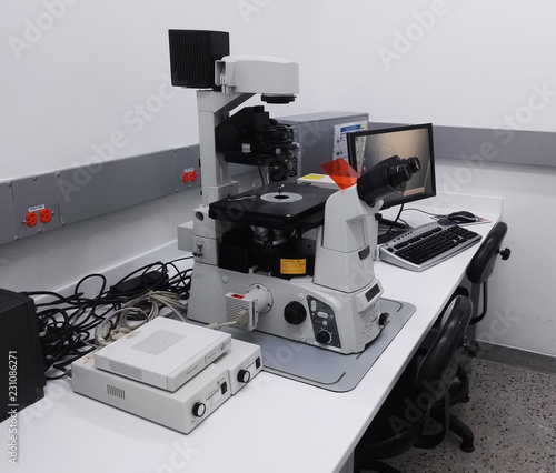 Desk with a high-tech microscopy station in a scientific laboratory. High magnification inverted fluorescence microscope, computer, electrical equipment and cables.