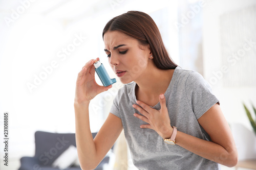 Young woman with asthma inhaler in light room