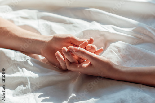 partial view of couple in live holding hads while lying in bed together