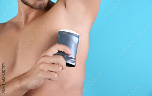 Young man using deodorant on color background, closeup. Space for text