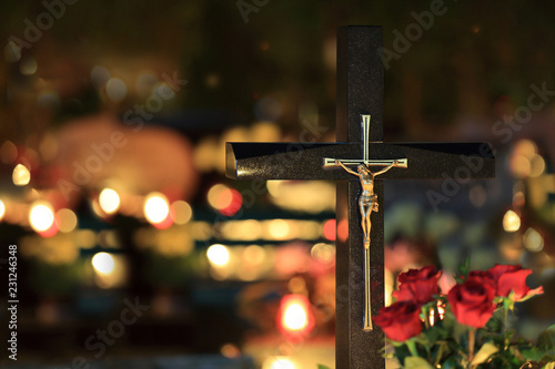 Piękny złoty wizerunek chrystusa na krzyżu na cmentarzu nocą w świetle palących się zniczy.