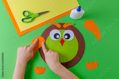kid is making a owl with color paper, glue and scissors, on green