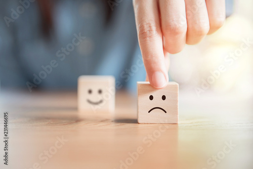 Close up customer hand choose sad face and blurred smiley face icon on wood cube, Service rating, satisfaction concept.