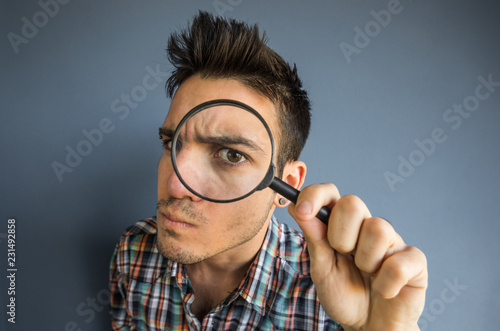 Funny man of a casual man looking though magnifyng glass on a grey background