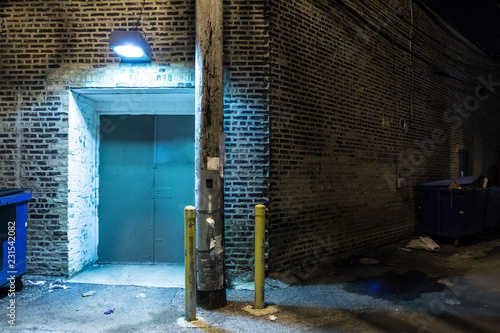 Dark and scary downtown urban city street corner alley with an eerie vintage industrial warehouse factory entrance and dirty dumpsters at night