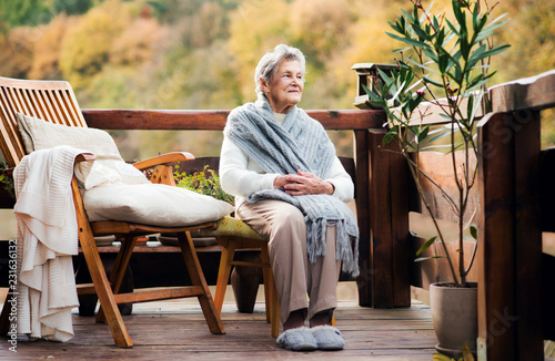 An elderly woman sitting outdoors on a terrace on a sunny day in autumn.