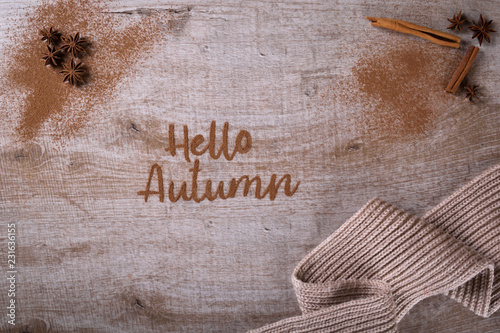 Hello, Autumn. The phrase is written on a wooden table with ground cinnamon among cinnamon sticks and badyan. Top view, flat lay