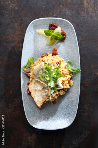 Ryba na risotto. Wykwintne danie obiadowe. Porcja ryby podana na risotto z suszonymi pomidorami.