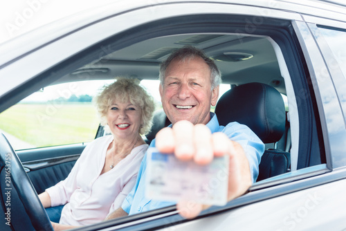 Portrait of a happy senior man showing his available driving license while sitting in the car next to his cheerful wife