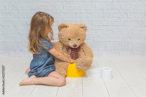 against the background of a white brick wall, the girl sits on a potty with the child, wiping her ass with toilet paper