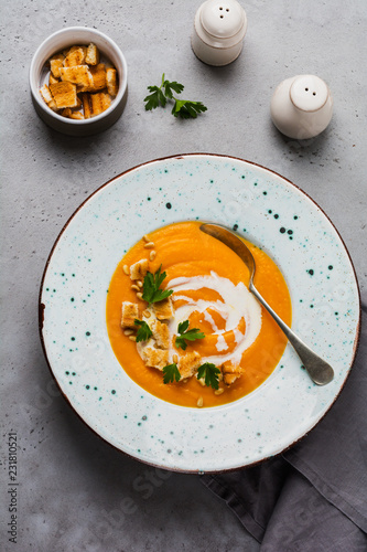 Pumpkin soup with cream, pieces of bread and cedar nuts in gray ceramic plate on gray table background. Traditional autumn food. Top view copy space.