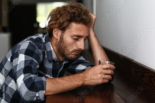 Depressed young man drinking alcohol in bar