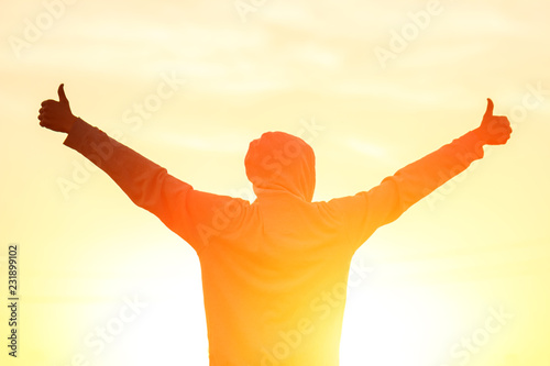 a man in the light of the sunset with his hands up, the concept of success, freedom and joy