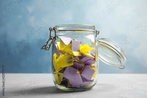 Colorful paper pieces for lottery in glass jar on color background