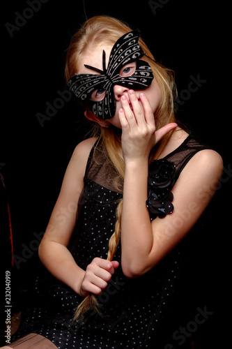Little girl in a masquerade mask on a black background.