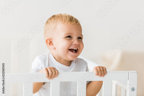 cheerful toddler standing in baby crib on white background