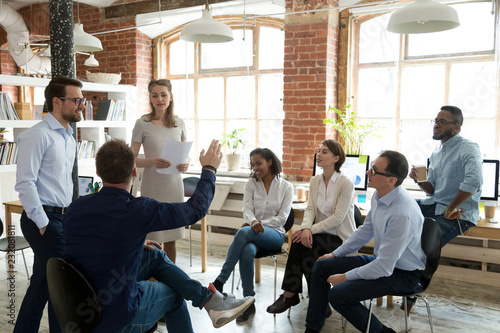 Ambitious male employee raise hand ask question to female presenter at meeting, man show activity at teambuilding with multiethnic colleagues, diverse workers brainstorm at office education briefing