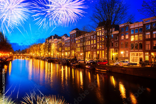 Houses over canal with lights and reflections at night with fireworks, Amsterdam, Netherlands,