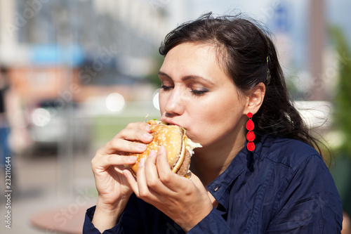 Beautiful girl with an appetite eating a hamburger on the street