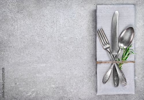 Table setting background with copy space. Concrete background with napkin, silverware and rosemary branch. Cutlery with fork, knife and spoon. Top view.