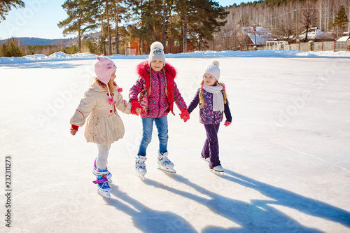 Three little girl friends learn to skate. Outdoor recreation and holidays