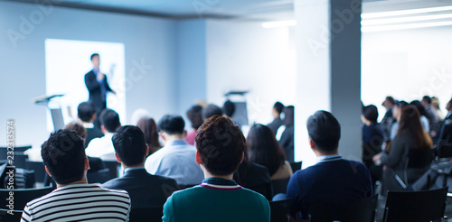 Presenter Presenting on Stage at Conference Meeting. Professional Lecture. Blurred De-focused Unidentifiable Presenter and Audience. Corporate Executive Manager Speaker. People Attendees