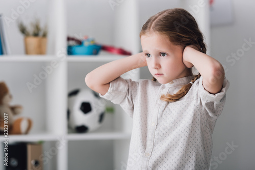 close-up portrait of sad little child covering ears with hands and looking away