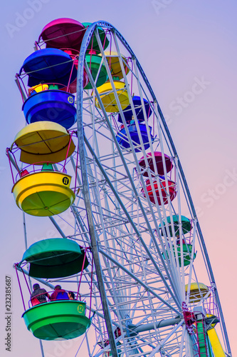 Ferris wheel with brightly colored multicolored cabins against the blue sky