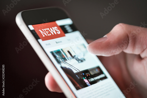 Mobile news application in smartphone. Man reading online news on website with cellphone. Person browsing latest articles on the internet. Light from phone screen.