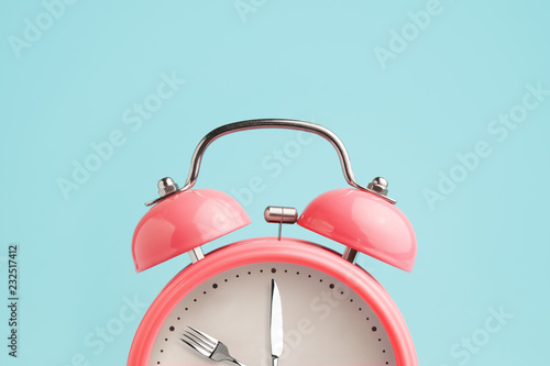 Alarm clock. Fork and knife instead of clock hands. Concept of intermittent fasting, lunchtime, diet and weight loss