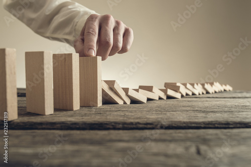 Businessman stopping collapsing wooden dominos