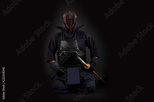 Kendo fighter holding and training with bamboo sword in studio on black background.