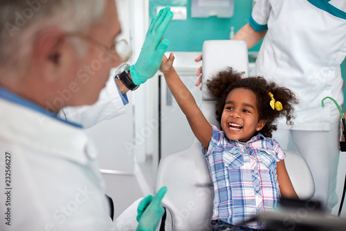 Cheerful young girl in dental chair making joke with male dentist