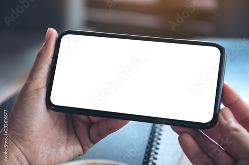 Mockup image of woman's hands holding and using a black mobile phone with blank screen horizontally for watching