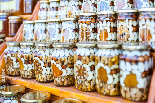 Different nuts, dried apricots and figs filled with honey in glass jars are on wooden shelves at the food exhibition