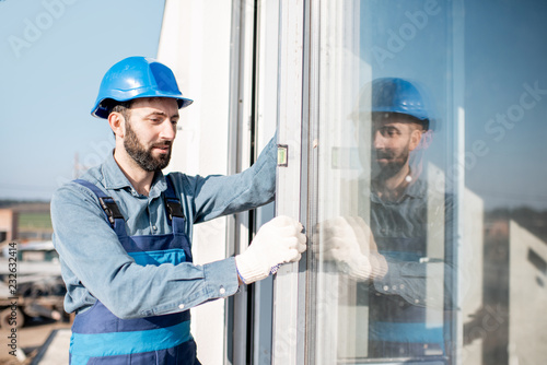 Workman in uniform mounting windows checking the level on the white building facade