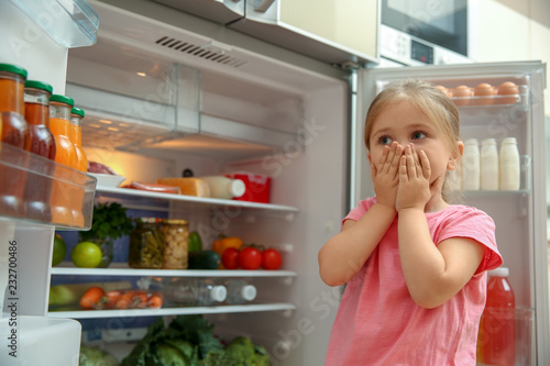 Little girl near bad smelling refrigerator at home