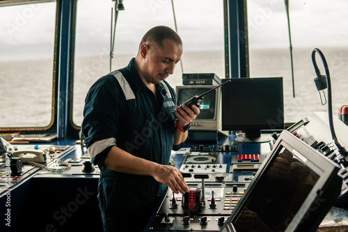 Marine navigational officer is changing speed ship or vessel during navigation watch. He speaks with engine room by walkie-talkie uhf radio