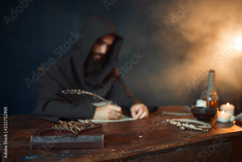 Medieval monk in robe writes with a goose feather